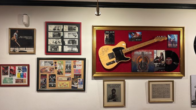Pared decorada con marcos de fotos y una guitarra eléctrica enmarcada.